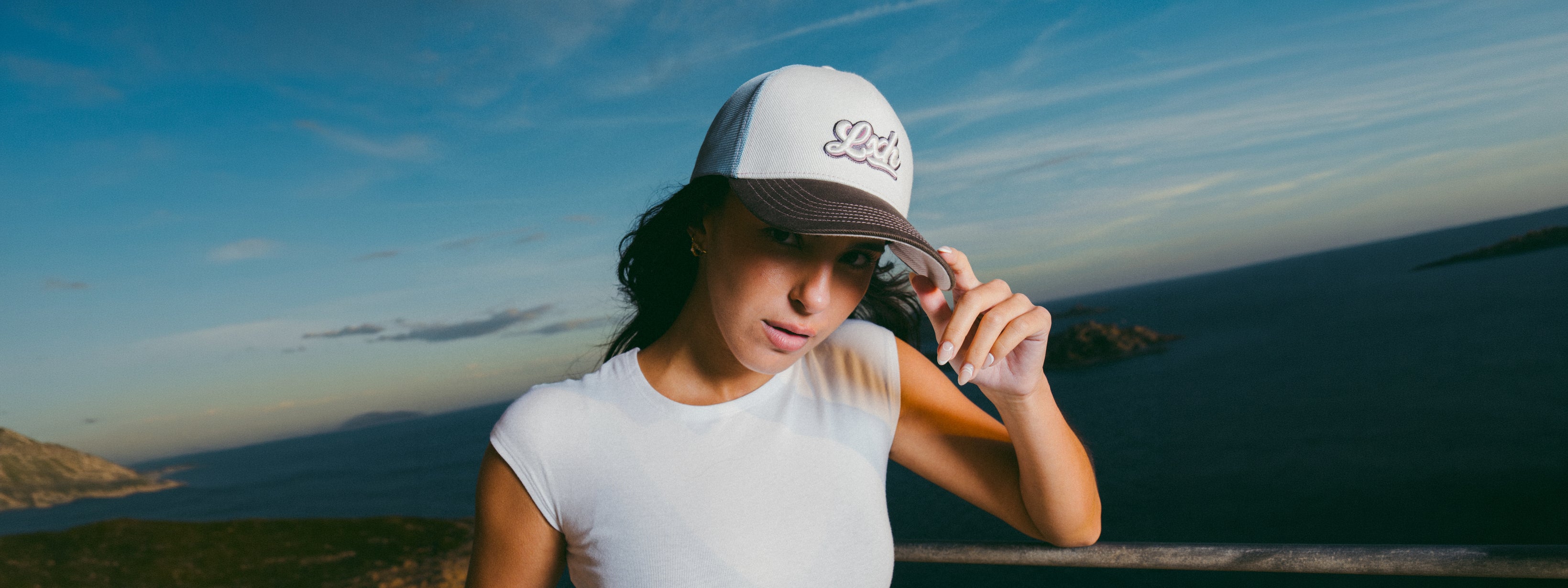 Femme portant une casquette trucker blanche assise près de la mer avec un vêtement jaune