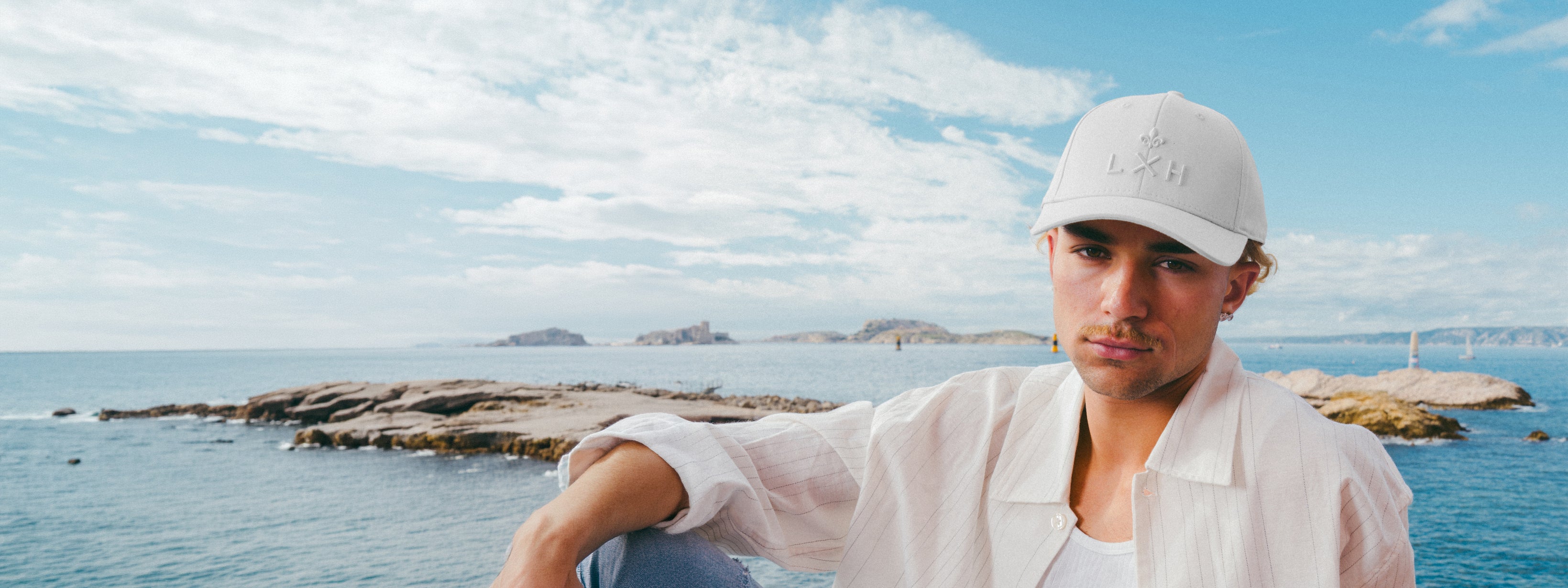 Homme portant une Casquettes Héritage blanche au bord de la mer avec paysage naturel en arrière-plan