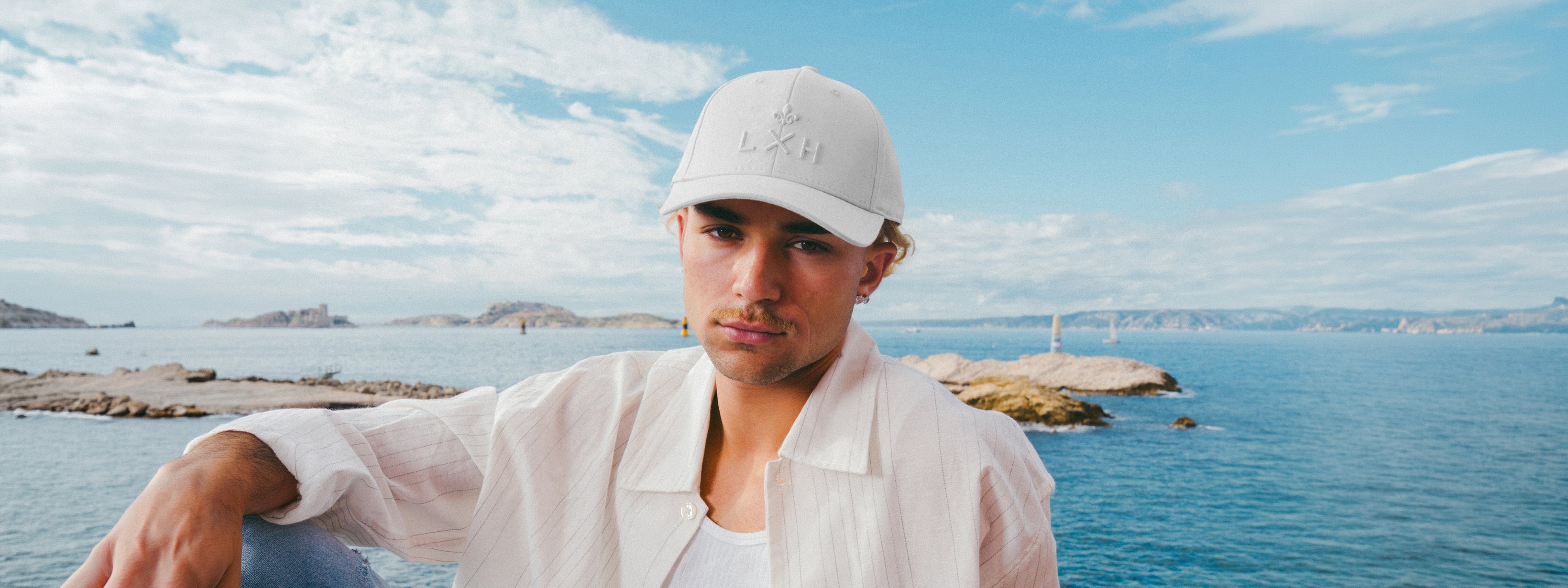 Homme portant une Casquettes Héritage blanche au bord de la mer avec paysage naturel en arrière-plan