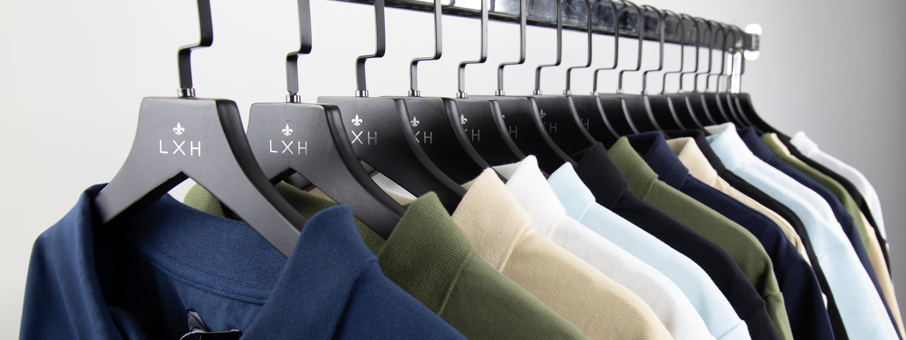 Collection de vêtements premium suspendus sur des cintres noirs dans une gamme de couleurs neutres et élégantes