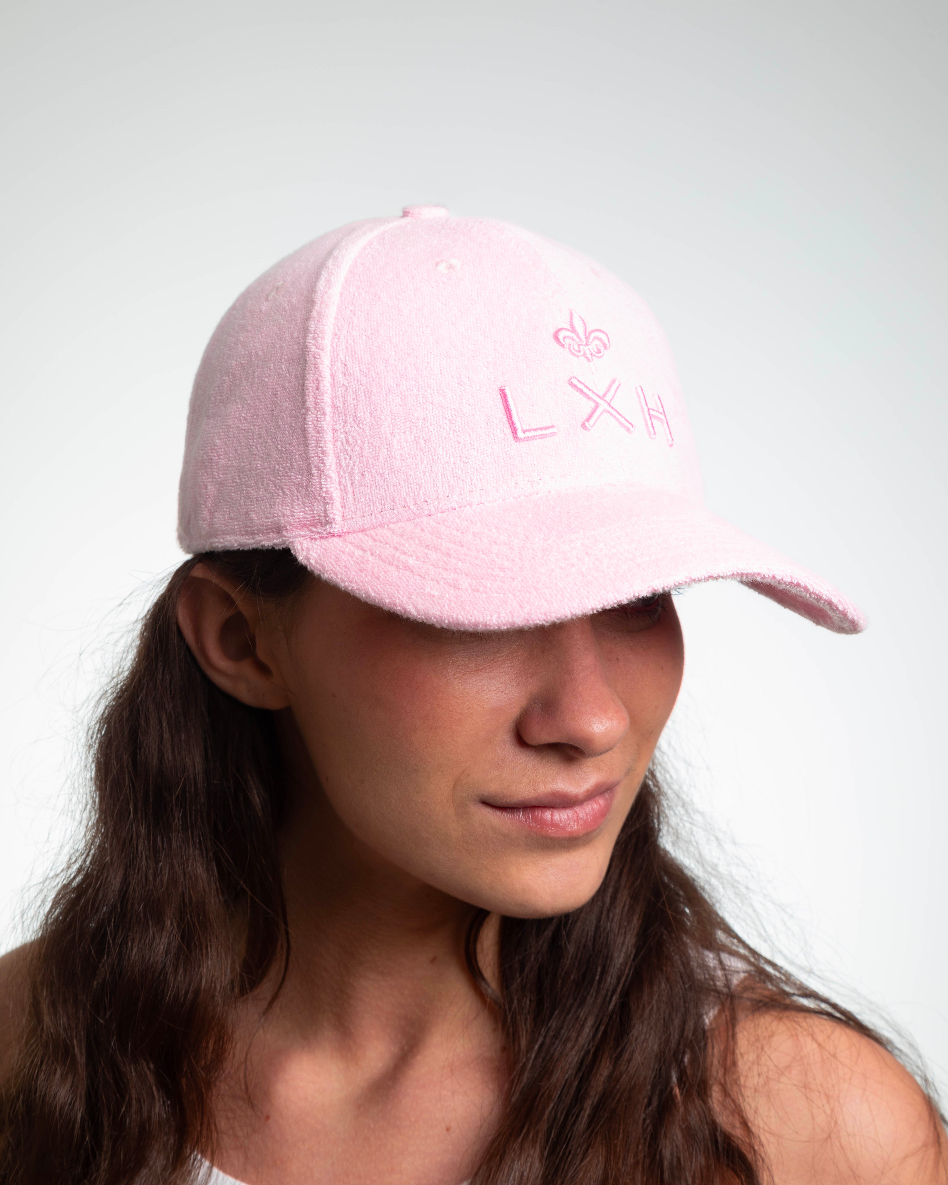 Profil d'une femme portant casquette LXH éponge rose pâle, broderie fleur de lys et logo LXH rose 3D sur la face avant.