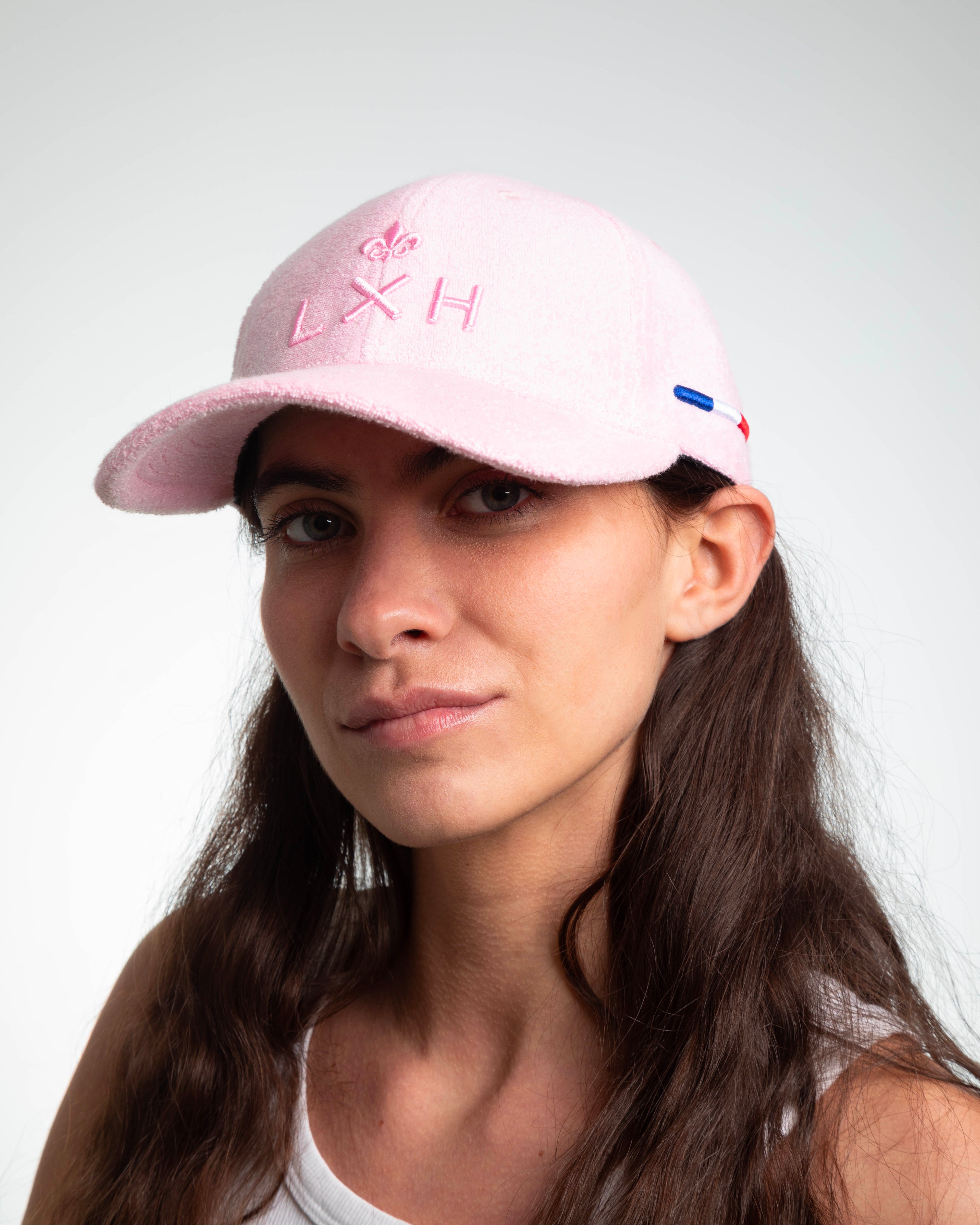 Femme brune portant casquette LXH éponge rose pâle, broderie fleur de lys et lettrage LXH rose 3D, languette tricolore.