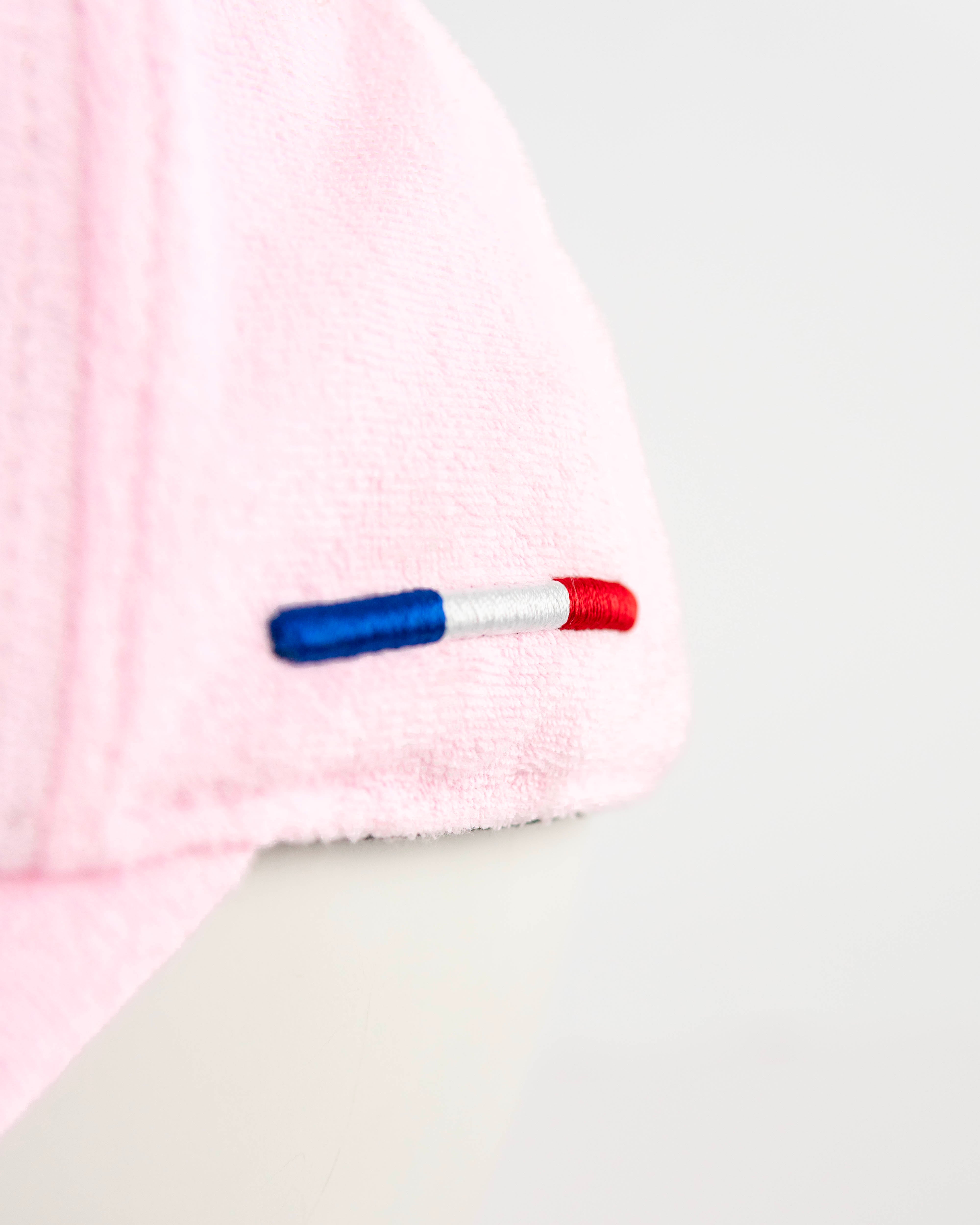 Détail tissu éponge rose pâle casquette LXH, gros plan languette tricolore brodée bleu blanc rouge sur côté gauche.