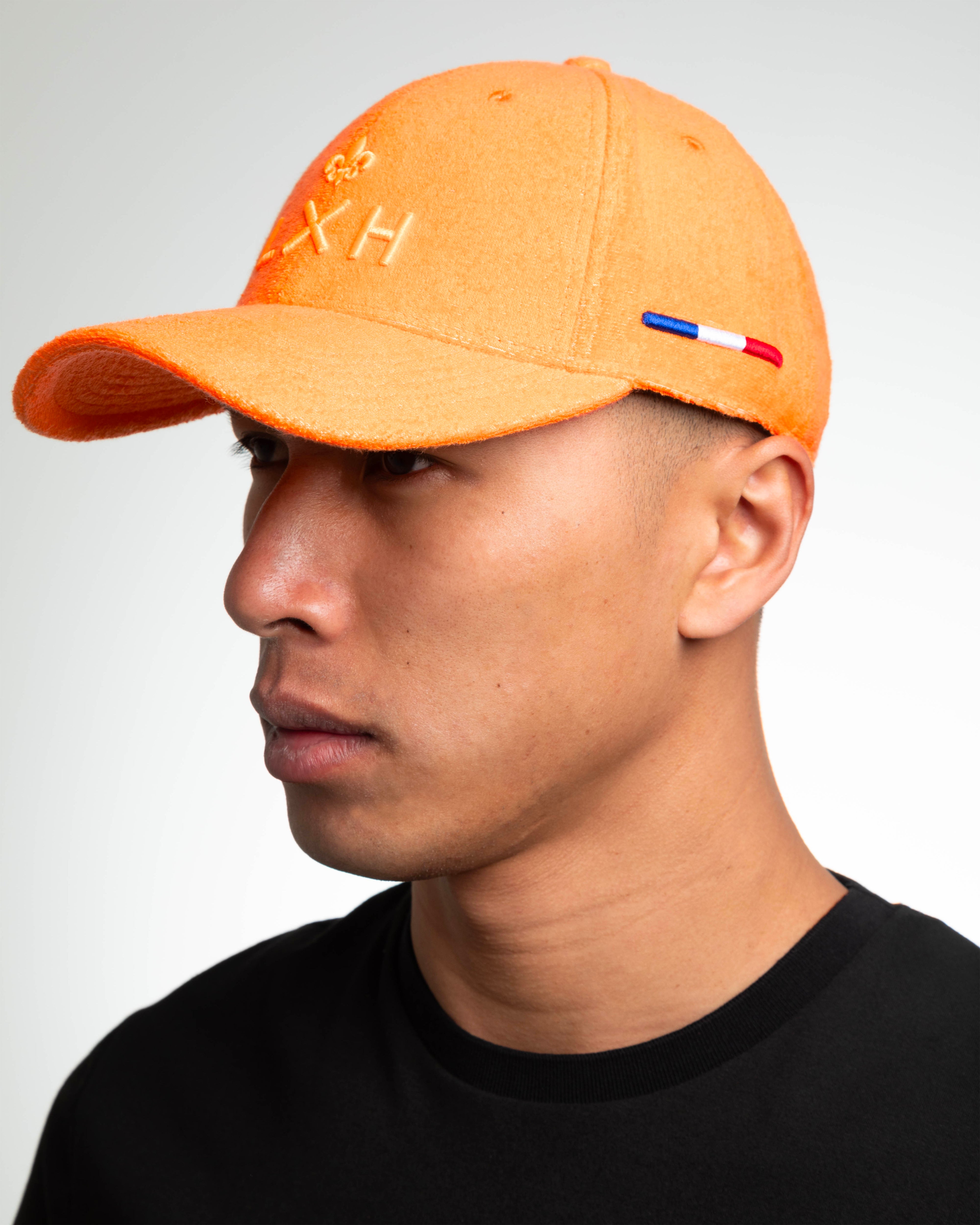 Casquette Héritage éponge orange portée par un mannequin, profil gauche, broderie LXH ton sur ton et liseré bleu blanc rouge.