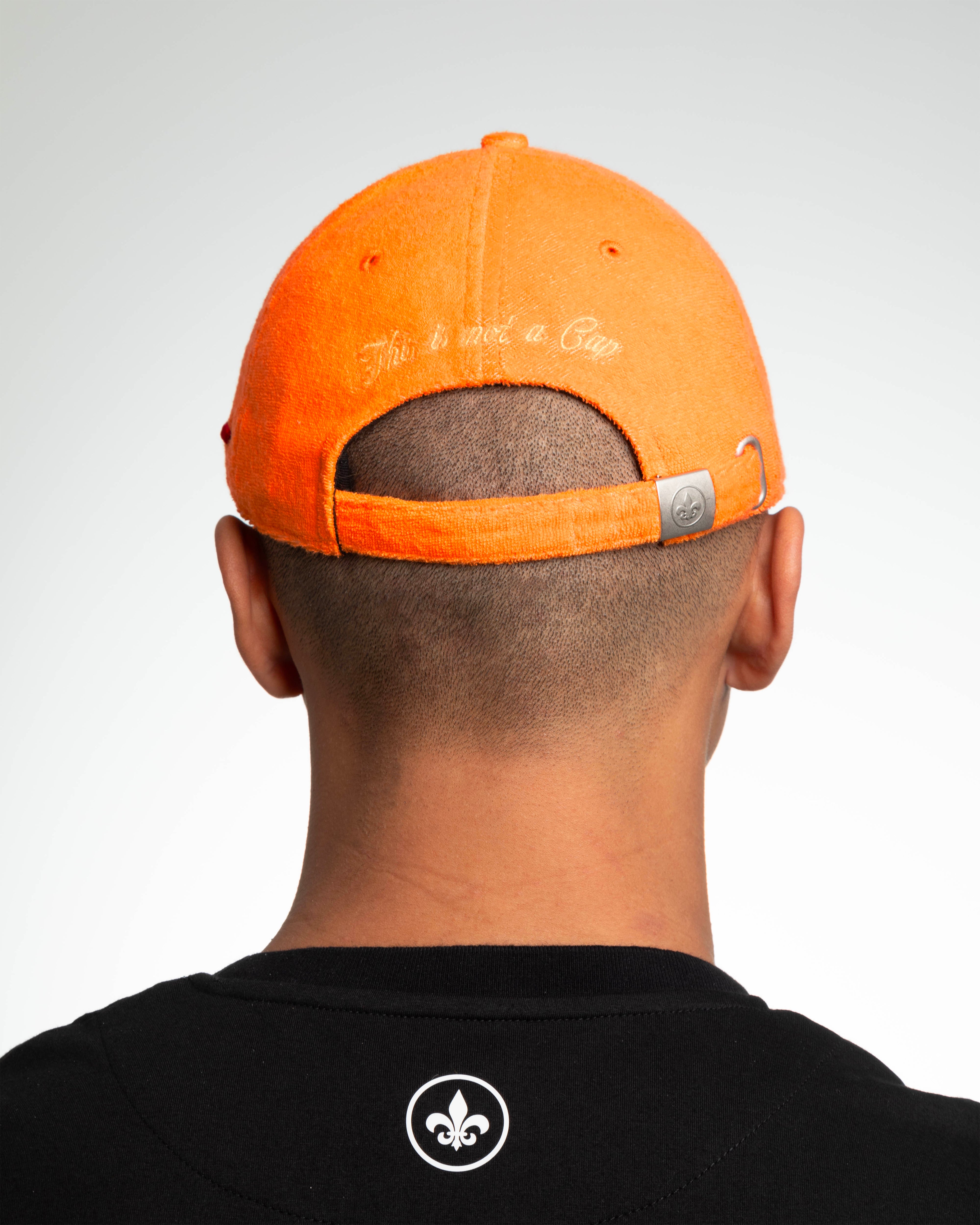 Casquette Héritage éponge orange vue de dos, broderie 2D « This is not a Cap » et attache métal embossée fleur de lys.