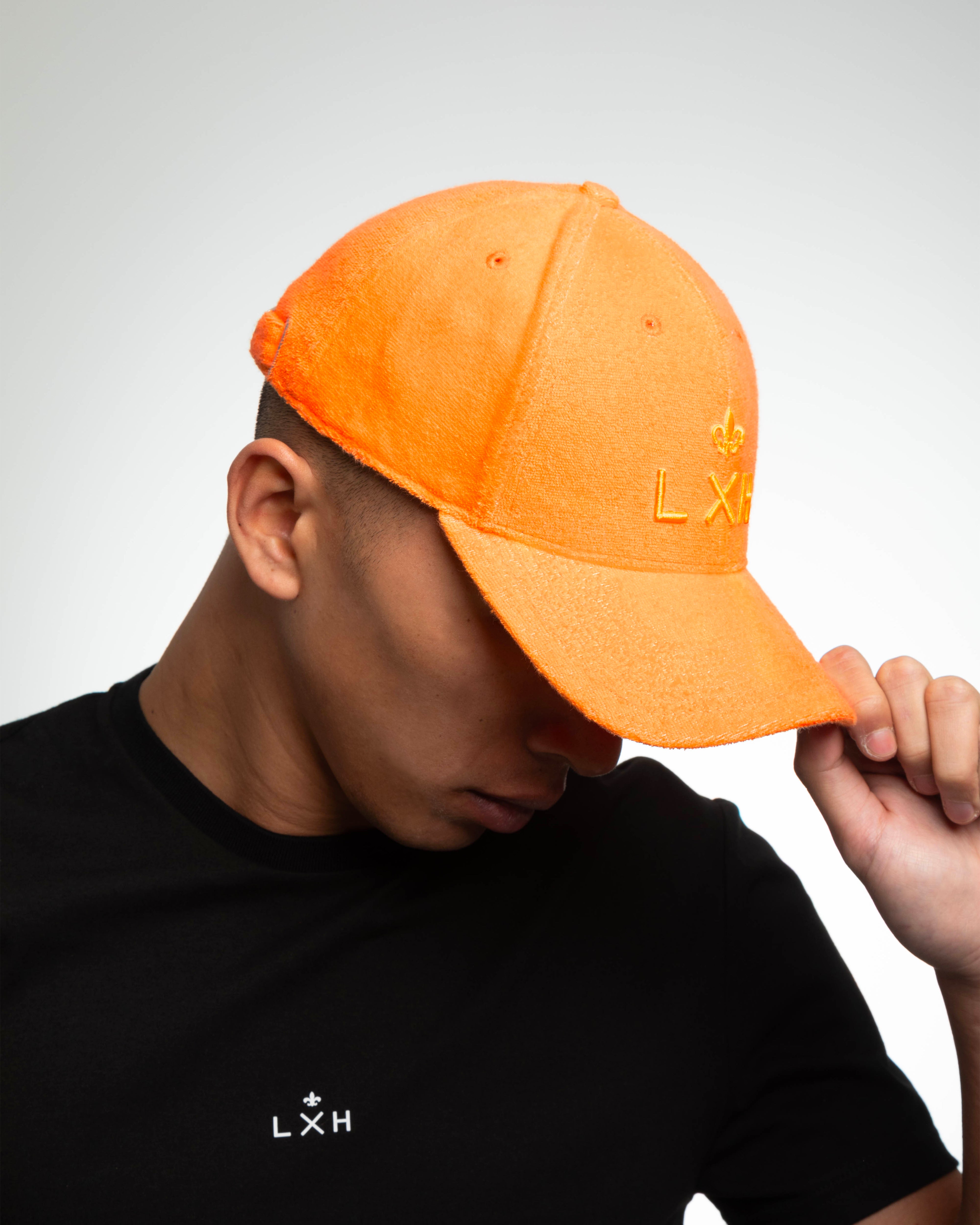 Casquette Héritage éponge orange portée inclinée visière baissée, texture bouclette estivale et broderie LXH ton sur ton.