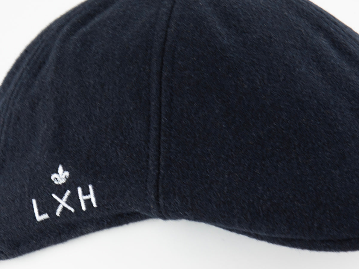 Détail du logo LXH brodé en blanc avec fleur de lys sur le panneau latéral du béret feutrine bleu nuit
