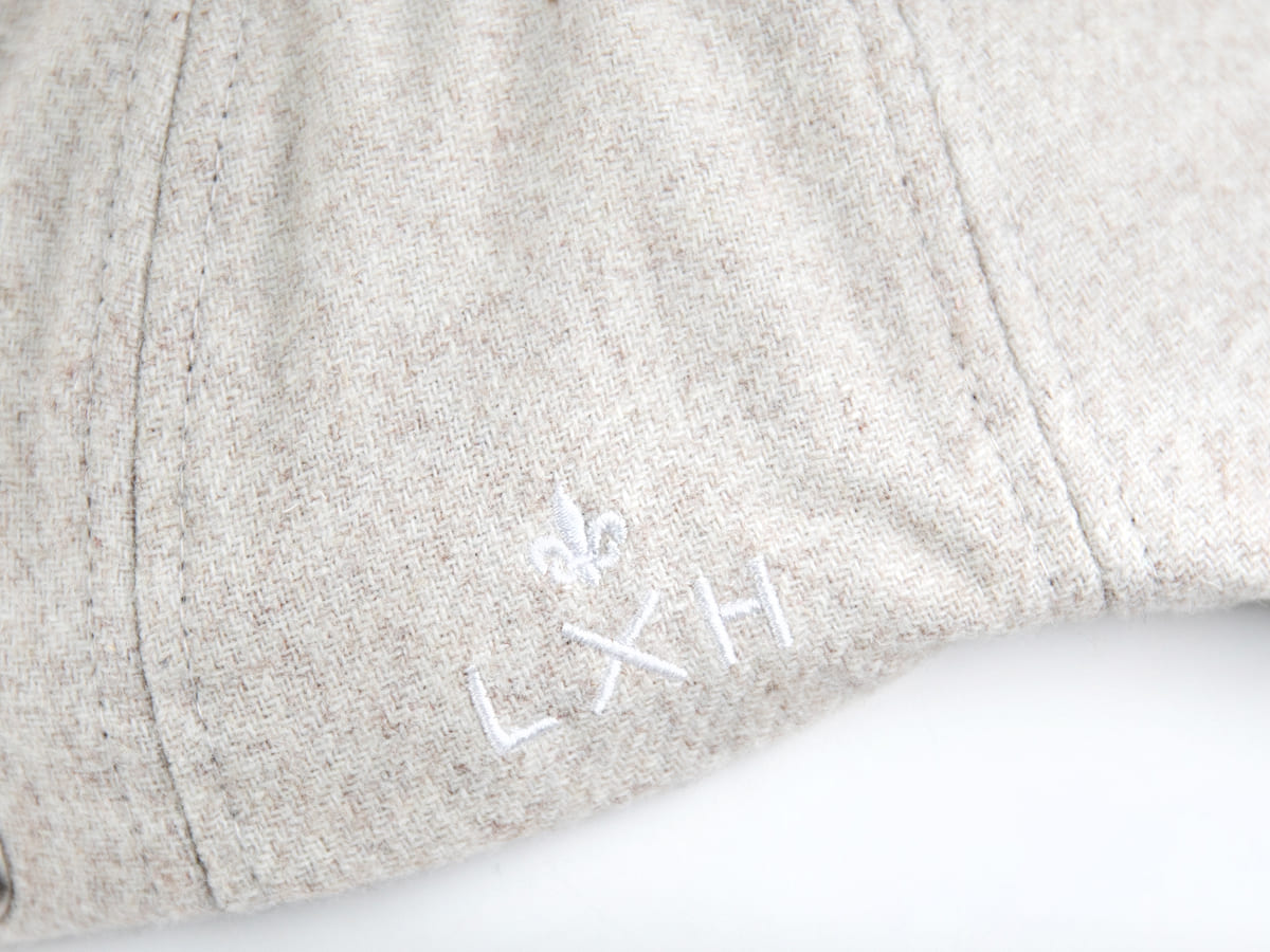 Macro tissu feutrine blanc cassé LXH, mailles laine chinée beige, broderie blanche fleur de lys au-dessus du sigle LXH.