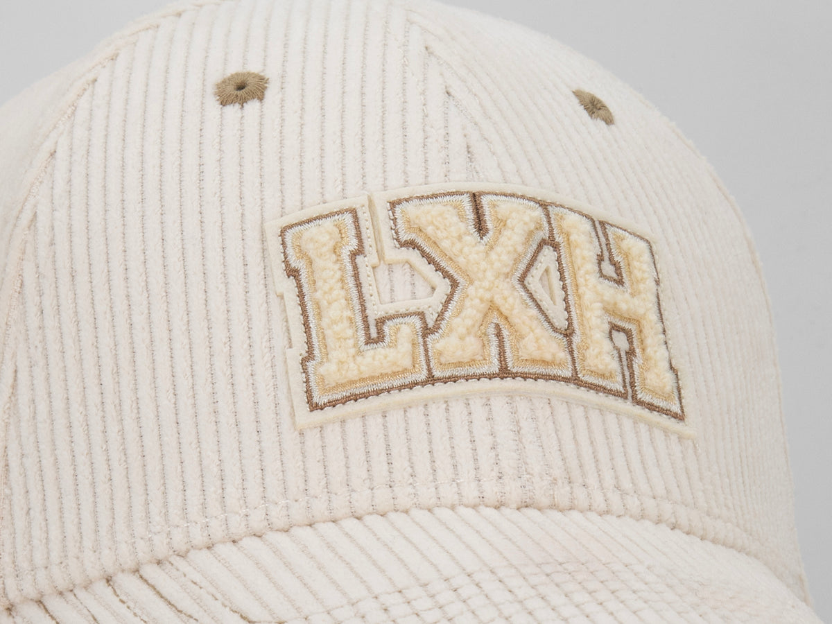 Macro patch chenille LXH varsity beige sur casquette Campus vanille, gros plan velours côtelé et broderie contour.