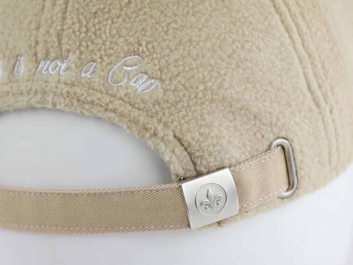Gros plan sangle réglable beige et boucle métal gravée fleur de lys, dos de la casquette LXH Héritage polaire.