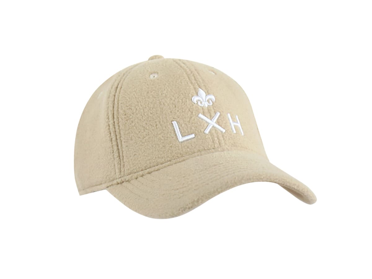 Casquette LXH Héritage polaire beige posée trois quarts face, fleur de lys et lettrage LXH brodés blanc sur polaire douce.
