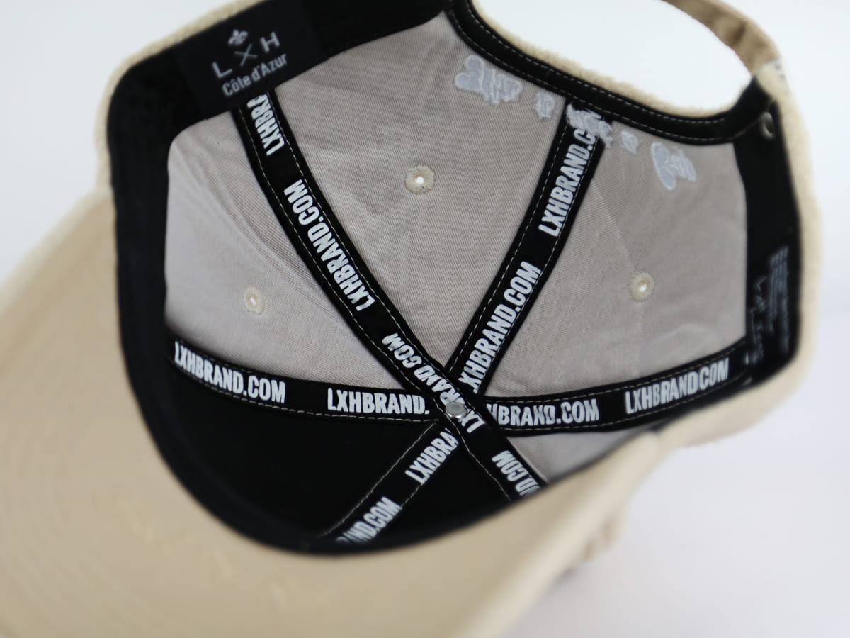 Vue intérieure rapprochée casquette LXH polaire beige, étiquette LXH Côte d'Azur et rubans LXHBRAND.COM en surpiqûre.