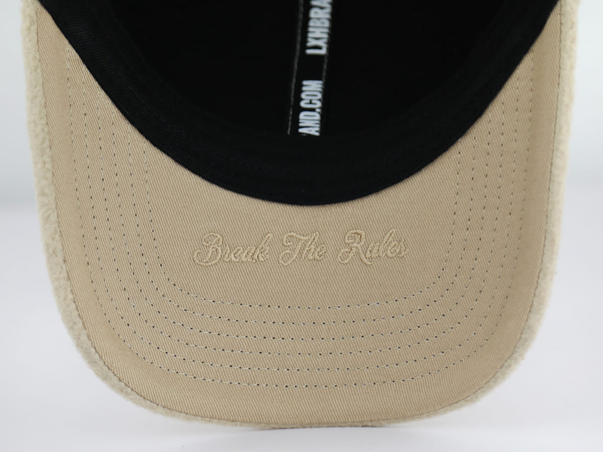 Détail de la broderie ton sur ton Break The Rules cousue sous la visière en coton beige de la casquette polaire Héritage LXH