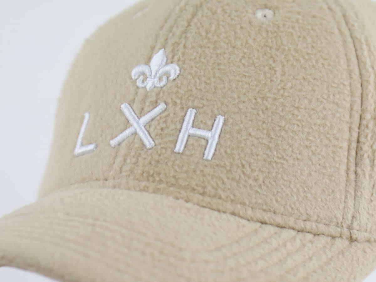 Zoom sur la broderie blanche fleur de lys et logo LXH cousue sur la face avant de la casquette polaire beige Héritage LXH