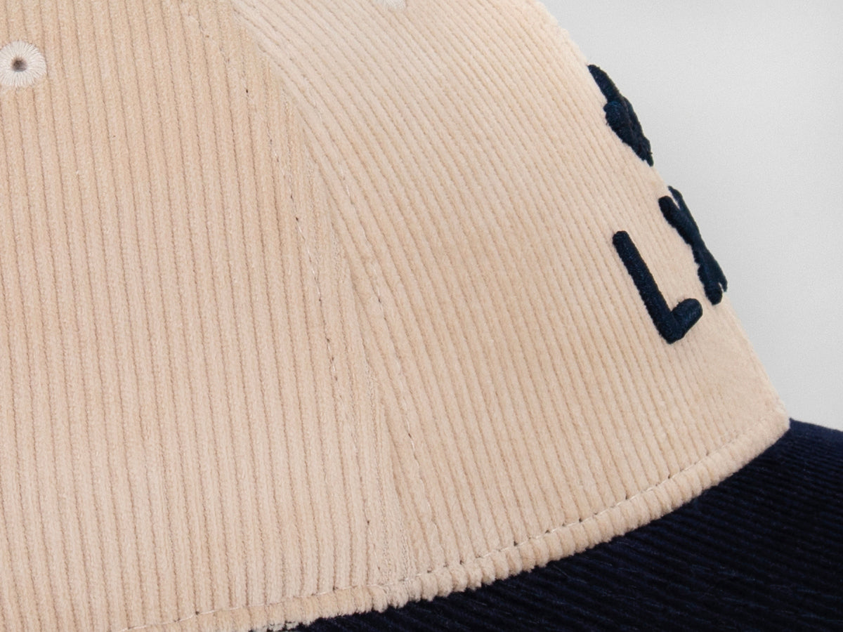 Détail couture casquette LXH Héritage, panneaux beige et jonction nette avec visière bleu marine en velours côtelé.