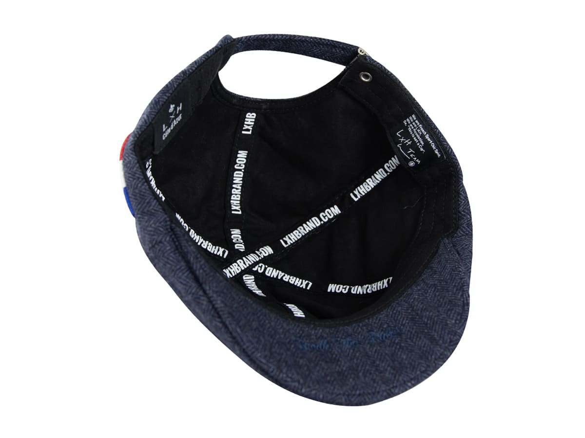 Intérieur du béret plat LXH chevron bleu marine avec doublure noire, sangles imprimées LXHBRAND.COM et étiquette de marque.