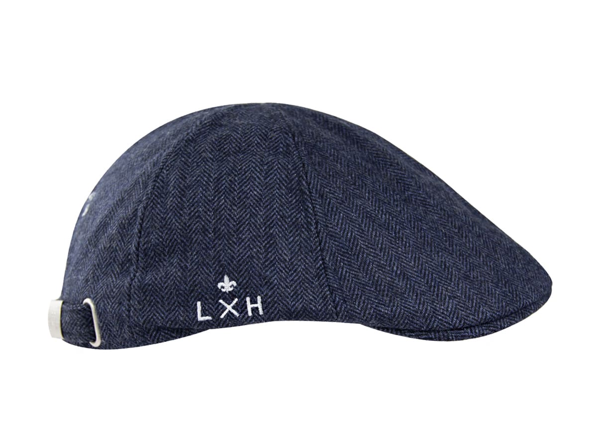 Profil droit du béret plat LXH bleu marine, détail du logo brodé blanc fleur de lys et LXH sur tissu chevron texturé.