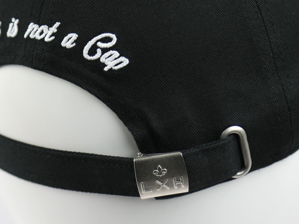 Détail de la casquette LXH en coton noir avec fermeture ajustable en métal et broderie blanche