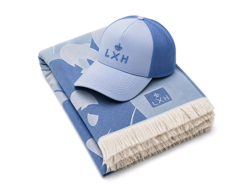Casquette Évasion LXH bleu topaze posée sur une fouta à franges.