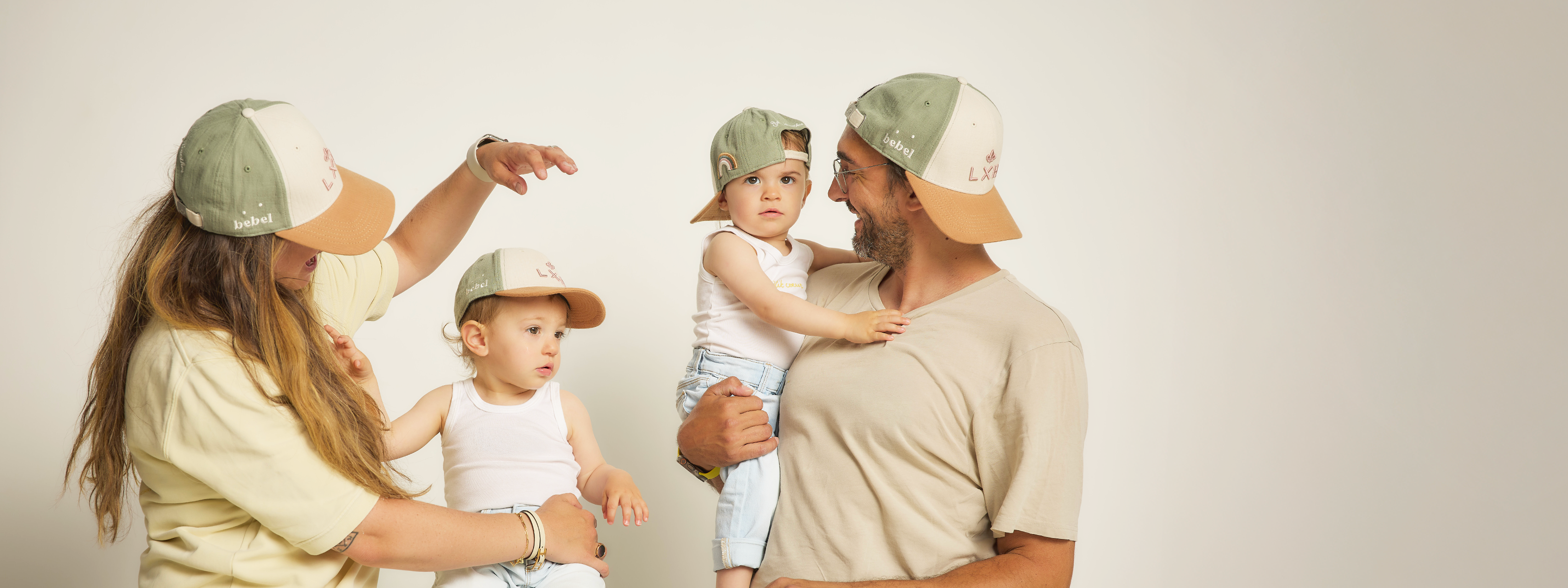 Famille portant des casquettes assorties posant ensemble dans un décor neutre pour un blog mode