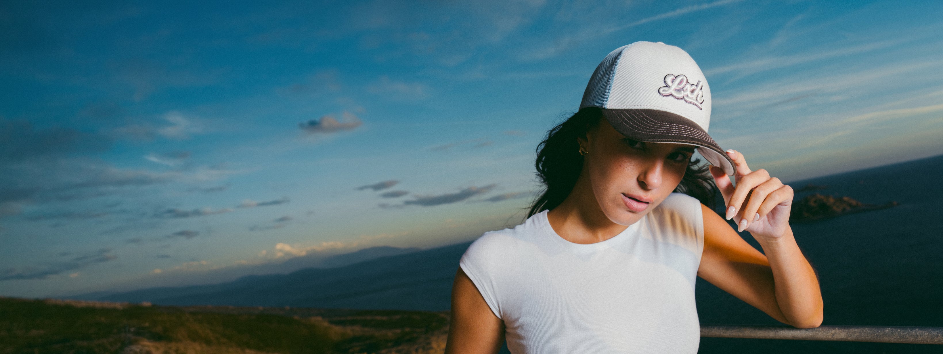 Femme portant une casquette trucker blanche assise près de la mer avec un vêtement jaune