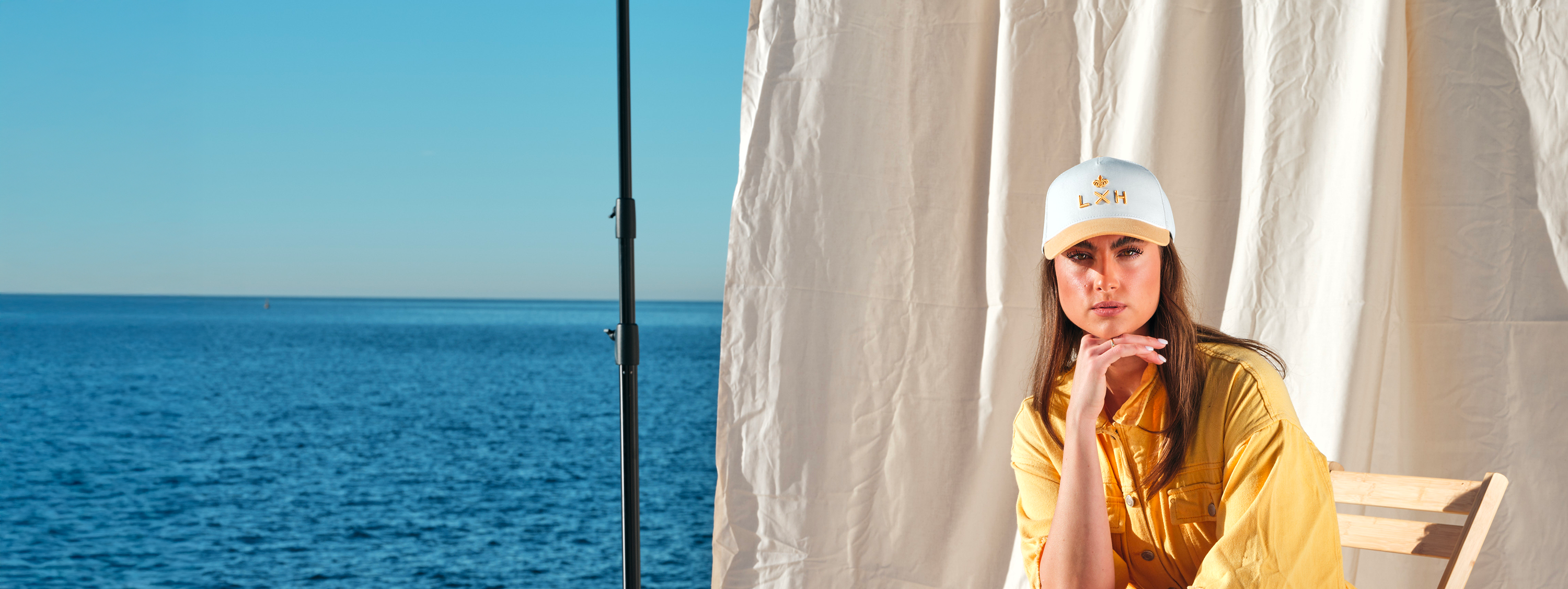 Femme portant une casquette trucker blanche assise près de la mer avec un vêtement jaune