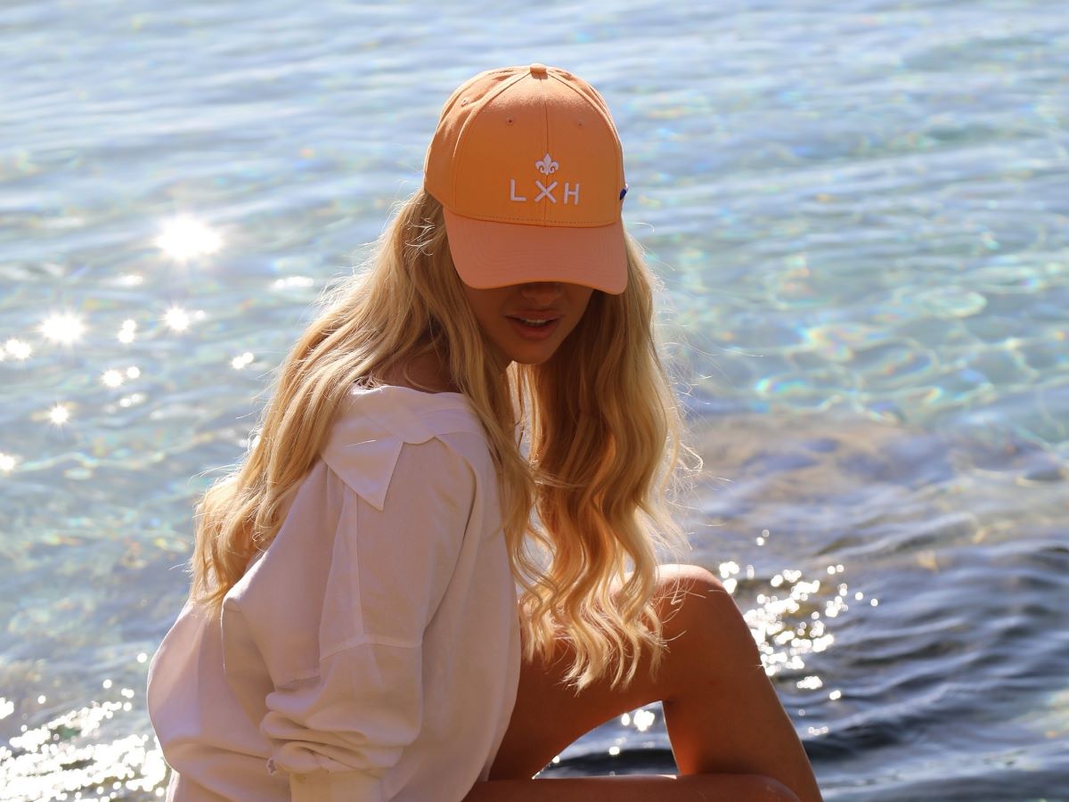 Casquette Coton Pêche LXH portée par une femme près de l'eau, avec des cheveux blonds ondulés