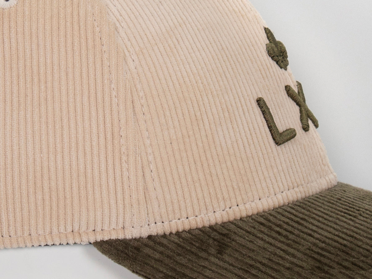 Plan rapproché jonction panneau beige côtelé et visière kaki, surpiqûres ton sur ton, broderie LXH en haut à droite.