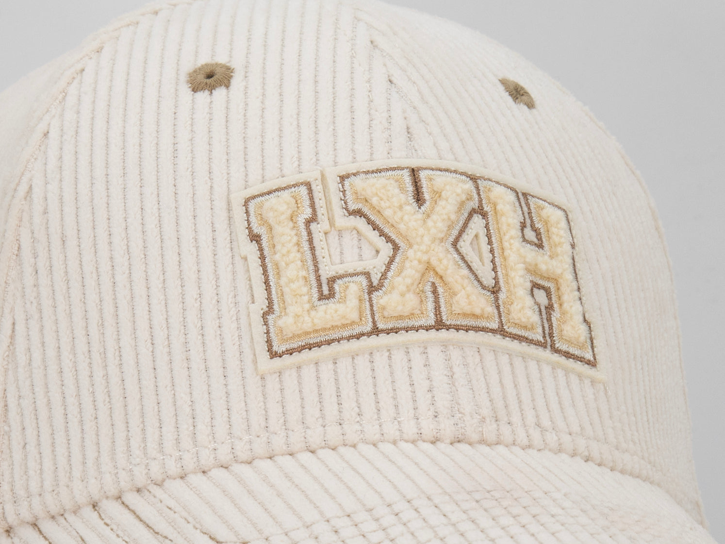 Macro patch chenille LXH varsity beige sur casquette Campus vanille, gros plan velours côtelé et broderie contour.