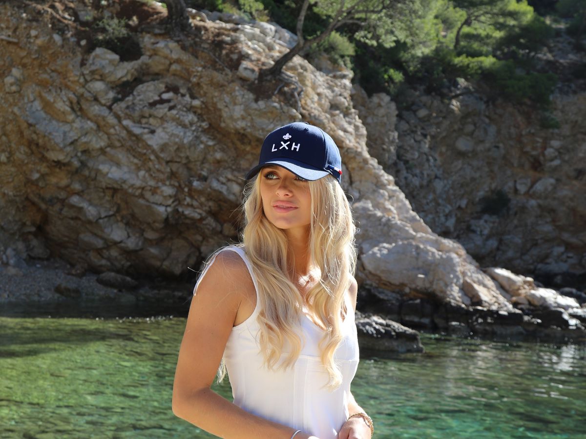 Casquette LXH en Coton Bleu Marine portée par une femme près de la mer avec un paysage rocheux en arrière-plan