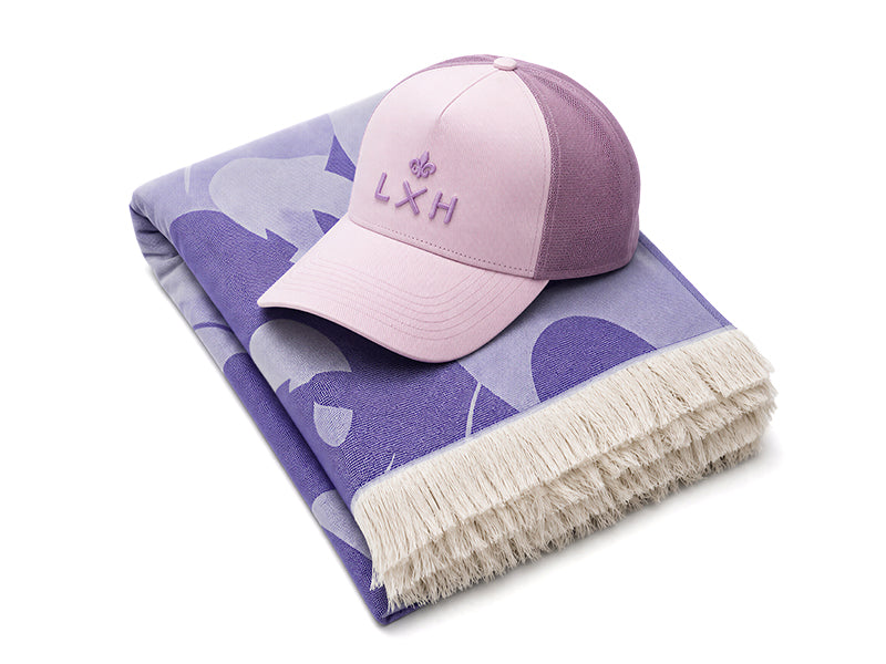 Casquette Évasion LXH rose quartz devant une fouta lilas à motifs.